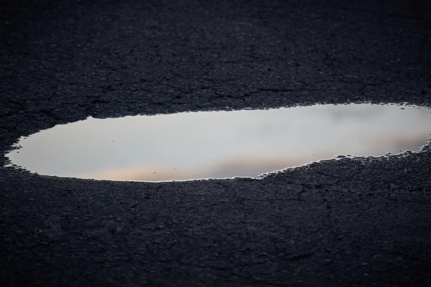 Close-up of a reflective puddle sitting in a crack on worn asphalt pavement.